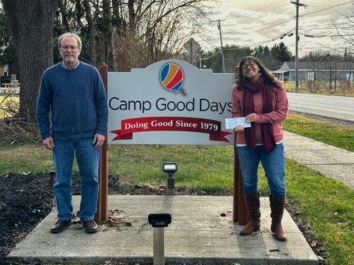 Photo of two people standing outside by a sign with text "Camp Good Days"
