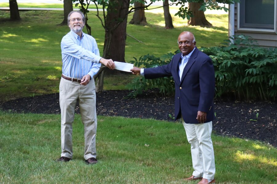 Two people standing on a lawn, holding a check