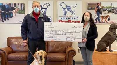Two people holding oversized check and a service dog. posters of America's Vet Dogs.