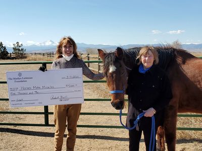 Two people with oversized check and a horse in a field.