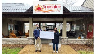 Two people holding oversized check outside Sunshine Campus building.