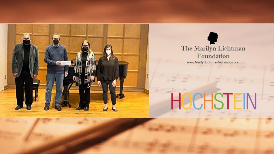 Four people standing with a check in front of a piano. Images of logo for The Marilyn Lichtman Foundation wwwMarilynLichtmanFoundation.org and HOCHSTEIN. Background graphic of sheet music.